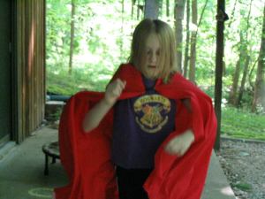 {Image is of the blogger at the age of ten. They have long blonde hair and are wearing a red cape. They are mid-jump.}